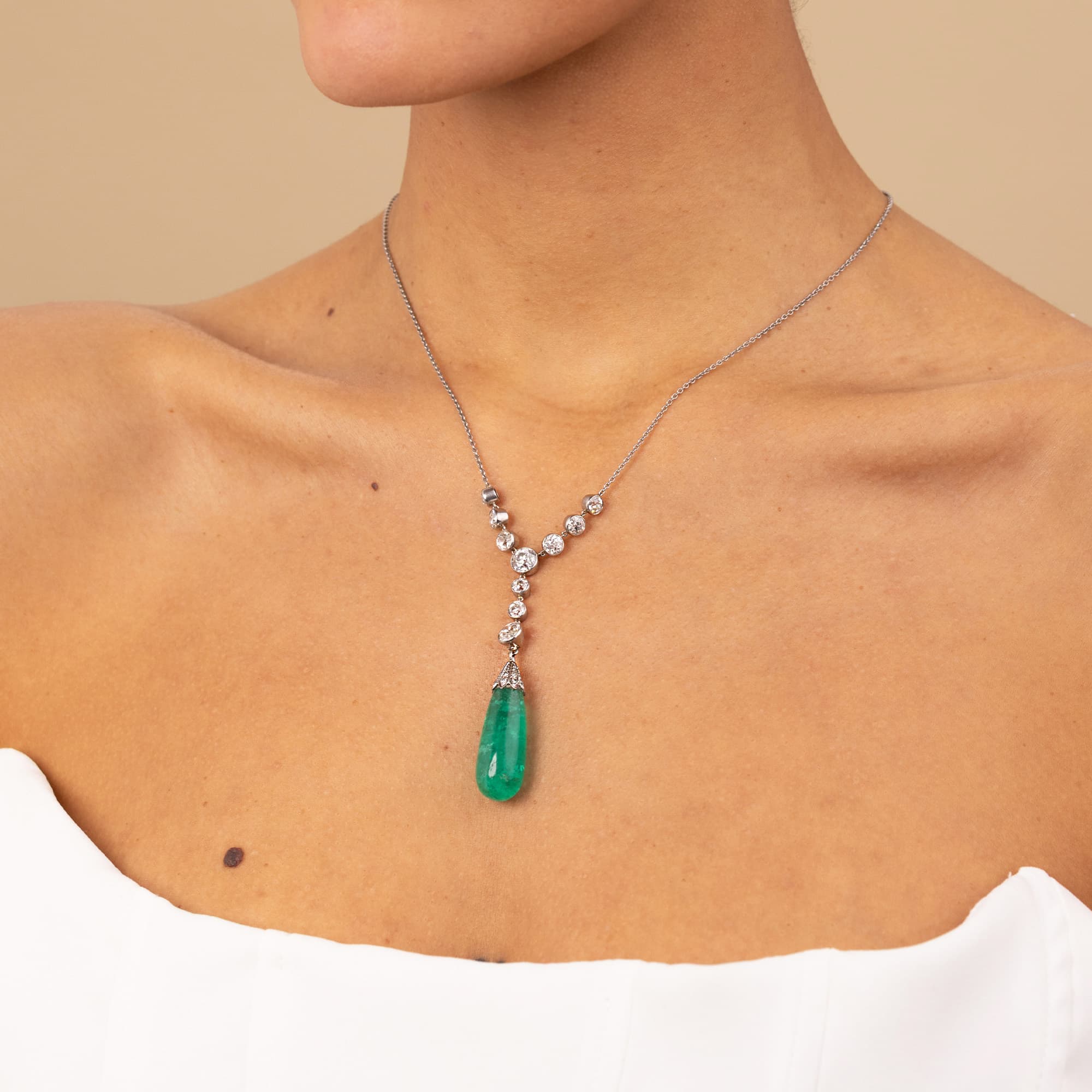 Necklace with a green Colombian emerald pendant worn by a person on a beige background