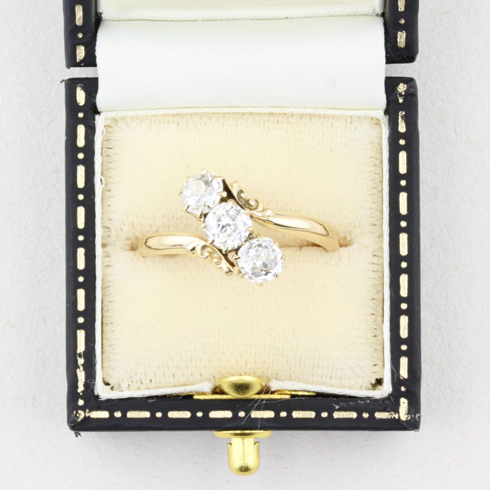Gold ring with three old cut diamonds in a decorative box on a white background