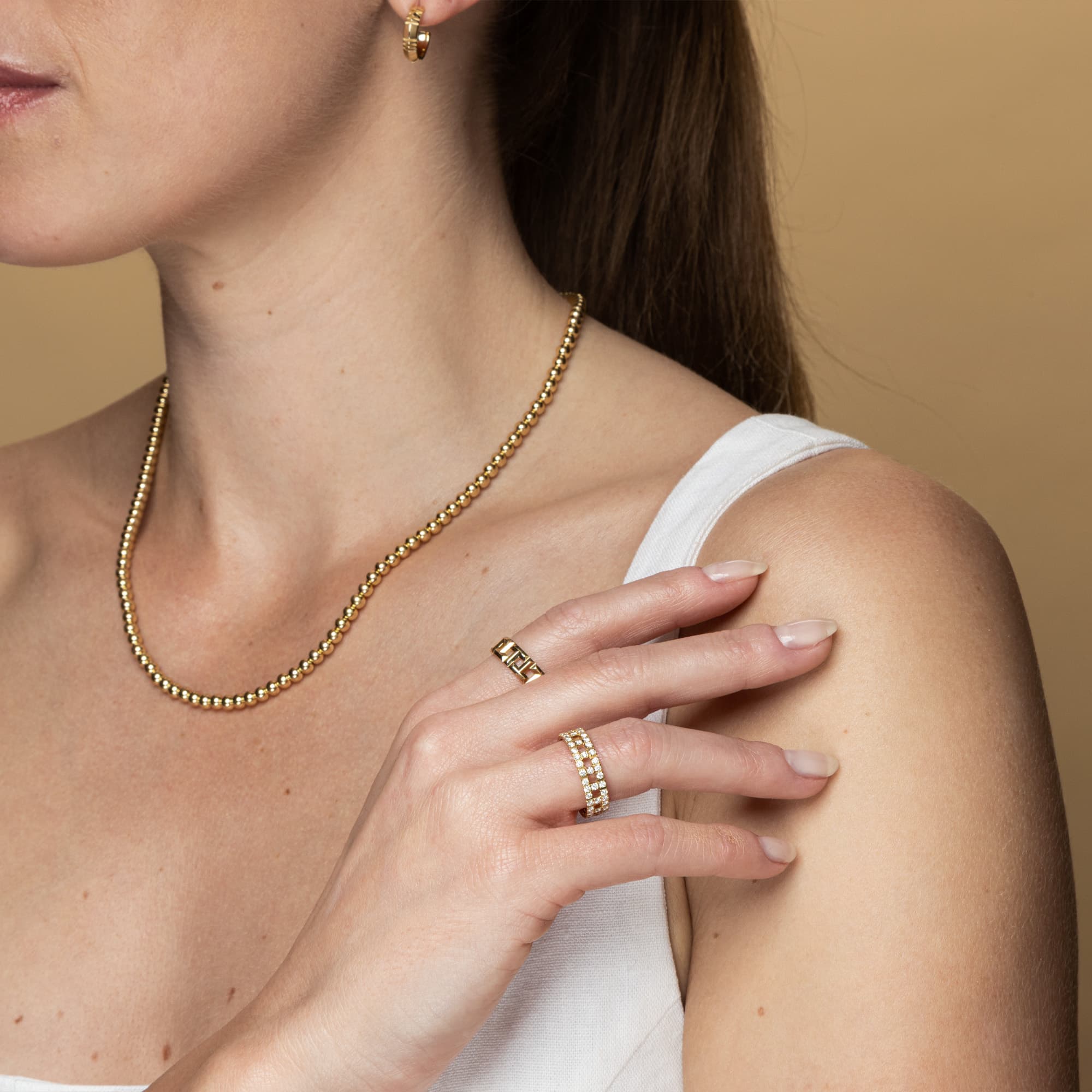 Woman wearing a gold necklace, ring, and earrings by Tiffany on a beige background