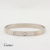 A Cartier Love bracelet in white-tone metal with five screw details and a central clear stone, shown on a white background with the Cartier logo at the bottom left.