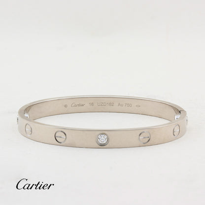 A Cartier Love bracelet in white-tone metal with five screw details and a central clear stone, shown on a white background with the Cartier logo at the bottom left.