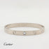 A Cartier Love bracelet in white-tone metal with five screw details and a central clear stone, shown on a white background with the Cartier logo at the bottom left.