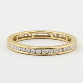 A yellow gold eternity ring featuring a continuous channel setting of round-cut diamonds on a plain white background.