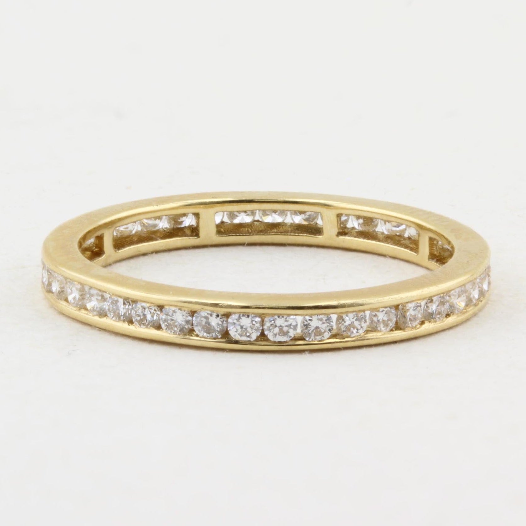 A yellow gold eternity ring featuring a continuous channel setting of round-cut diamonds on a plain white background.