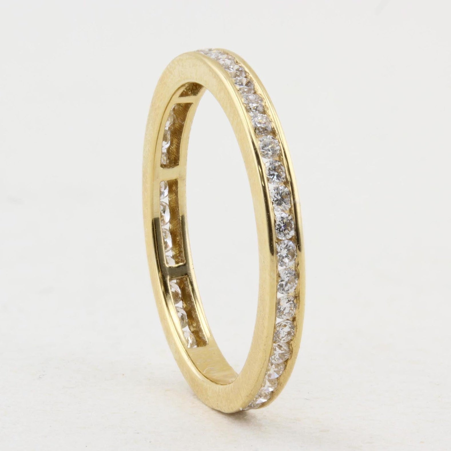 A yellow gold eternity ring featuring a continuous channel setting of small clear stones, shown standing upright on a plain white background.