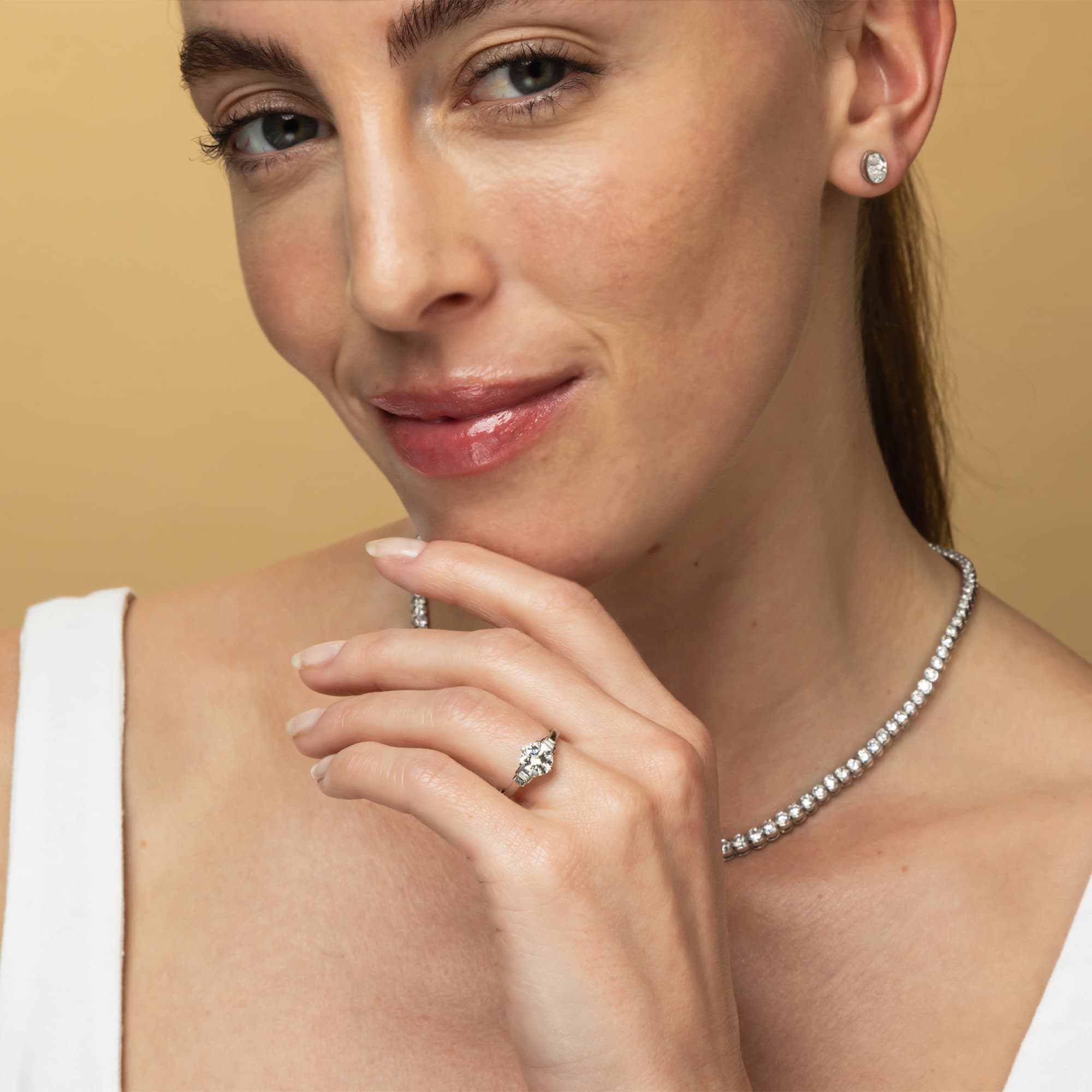 Woman wearing a diamond necklace, ring, and earrings on a beige background