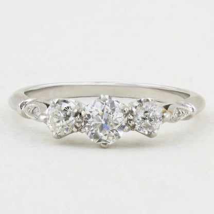 A white gold three-stone diamond ring with a central round diamond flanked by two smaller round diamonds, accented by small diamonds on the shoulders, set against a plain white background.